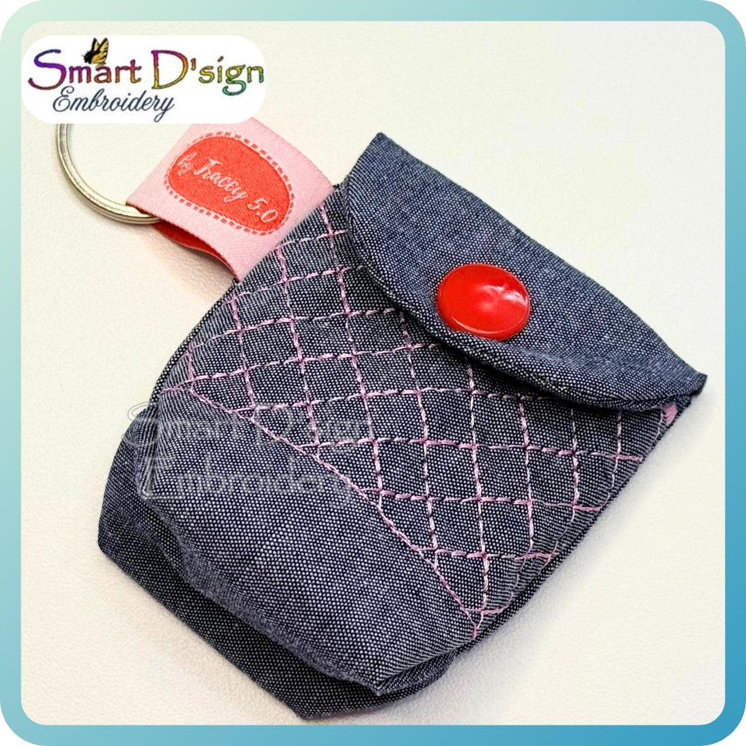 Denim keychain pouch with red button and pink stitching on a light background, branded 'Smart D'sign Embroidery'.