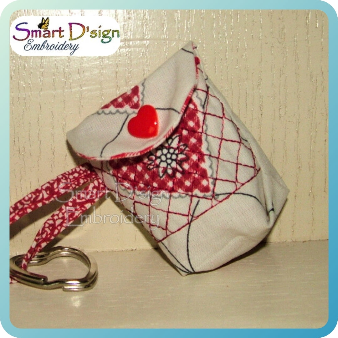 Fabric pouch with red heart and grid pattern, attached to a keychain, on a textured surface with 'Smart D'sign Embroidery' branding.