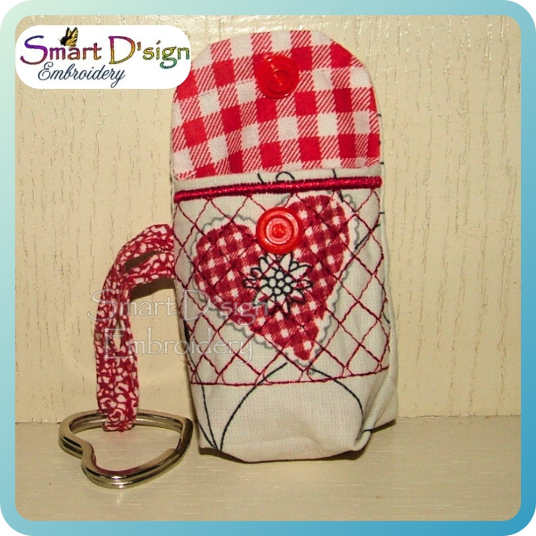 Fabric keychain with red and white checkered pattern and heart design on a wooden surface, branded 'Smart D'sign Embroidery'.